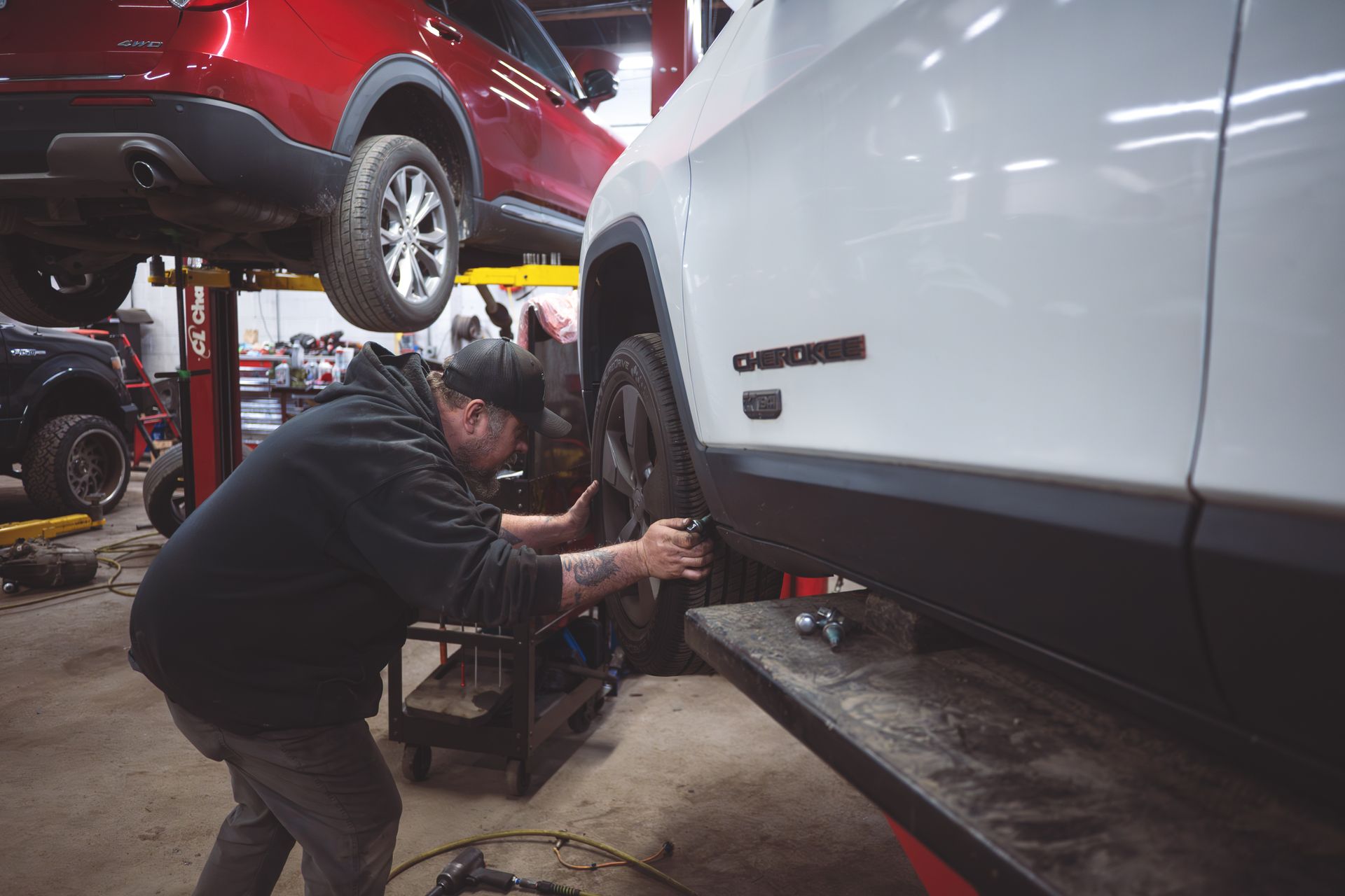 Mechanic working on the wheel of a white Jeep Cherokee raised on a lift in a garage | Musser Automotive