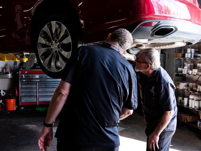 Service manager Dwayne and senior technician Ron inspecting the rear of a red vehicle on a lift at Musser Automotive.