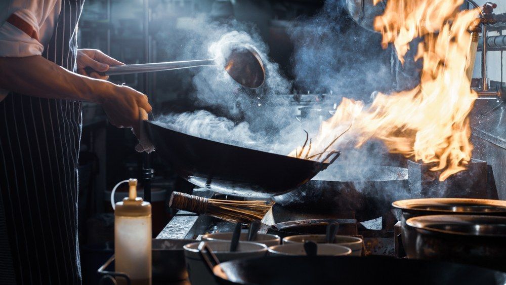 A Chef is Cooking Food in a Wok on a Stove With Flames Coming Out of It — Kowin Restaurant in Taree, NSW