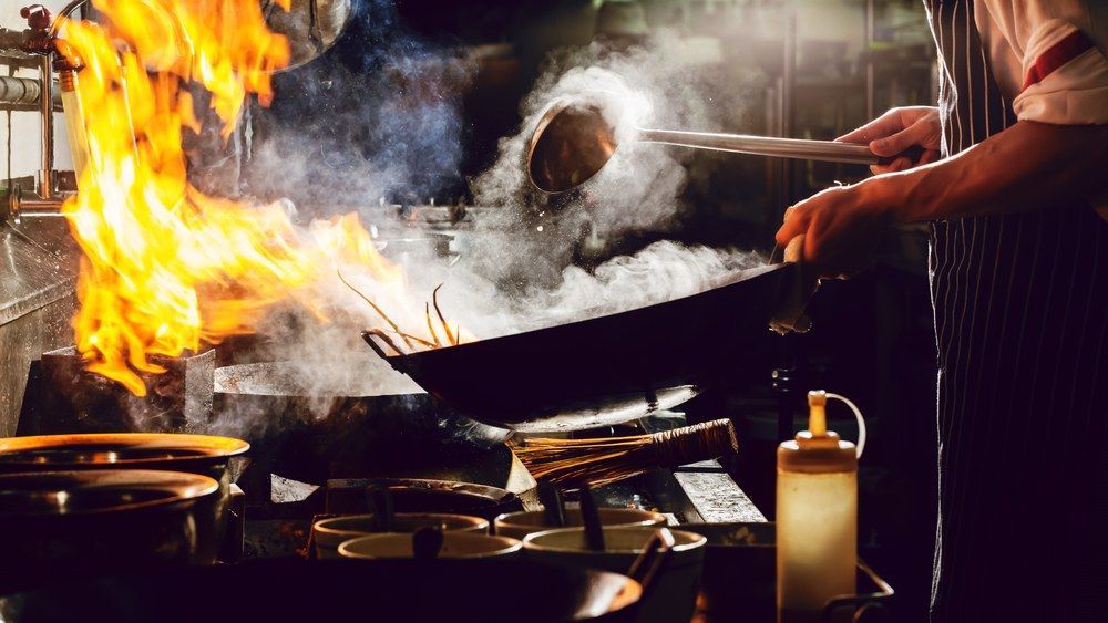 A Chef is Cooking Food in a Wok in a Restaurant Kitchen — Kowin Restaurant in Harrington, NSW