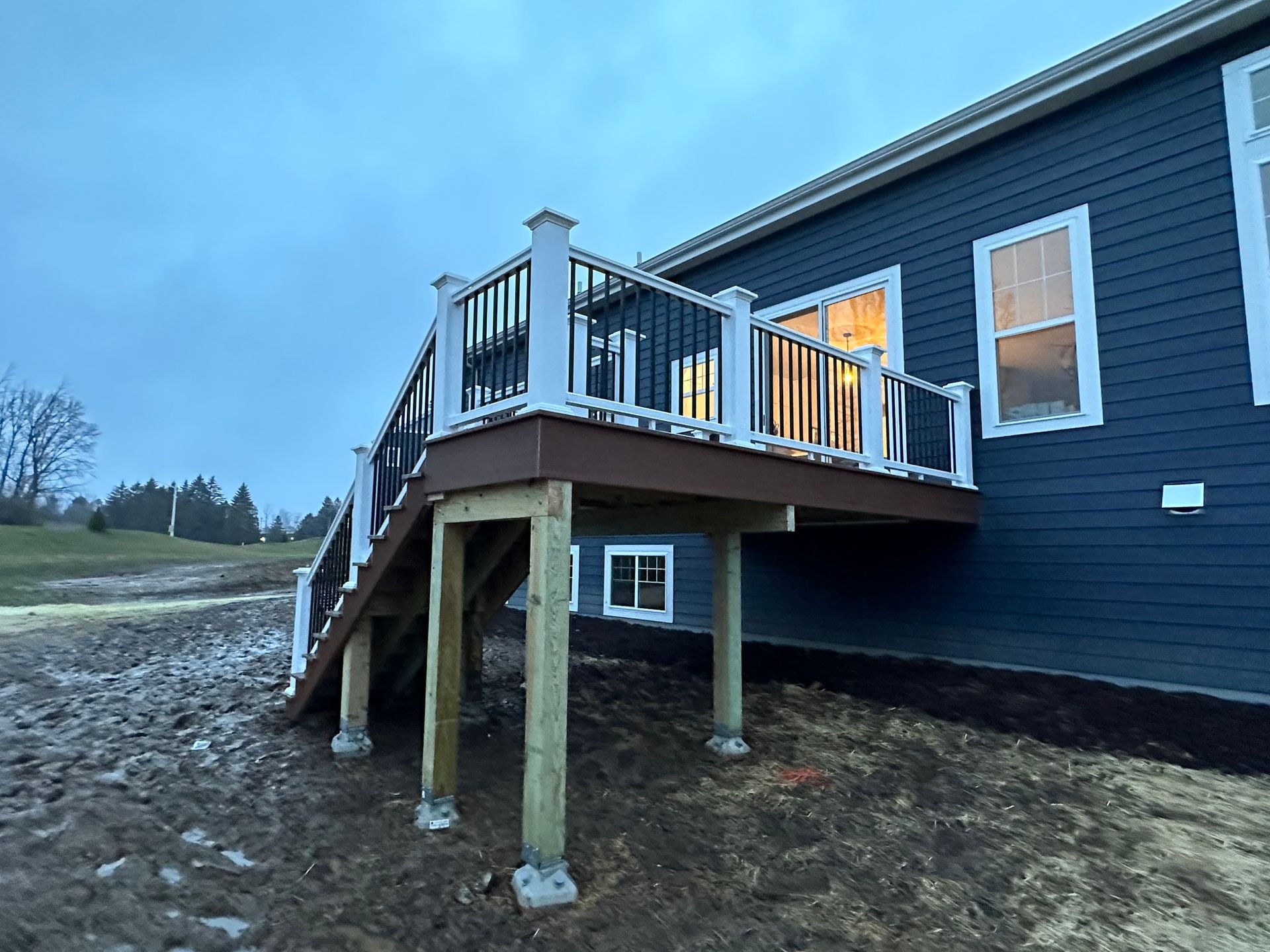 Newly constructed deck with stairs attached to a dark blue house. White railings and brown decking.