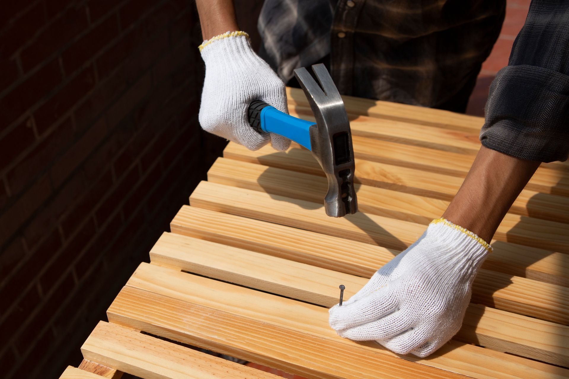 Gloved hands using a hammer and nails to assemble a wooden slatted bench