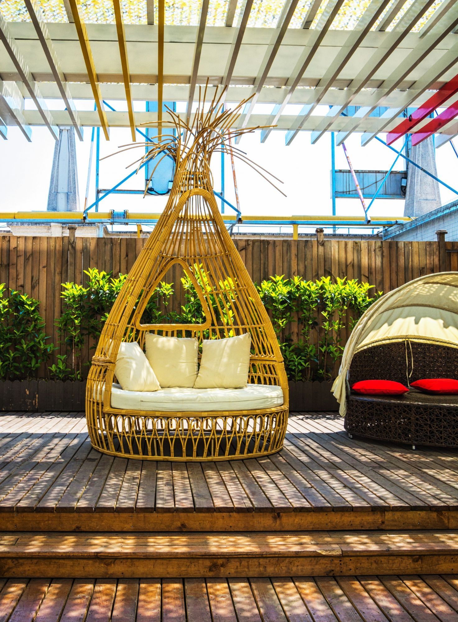 Wicker chair with cushions on a wooden deck, outdoor setting with a second lounge chair and greenery.