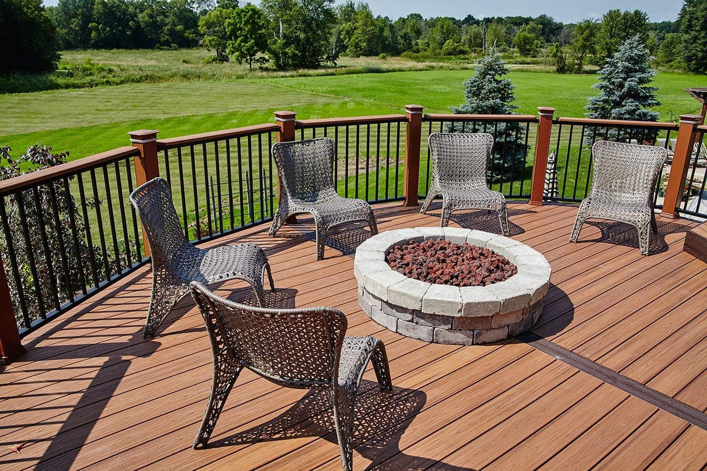 Deck with fire pit and six wicker chairs, overlooking a green field.