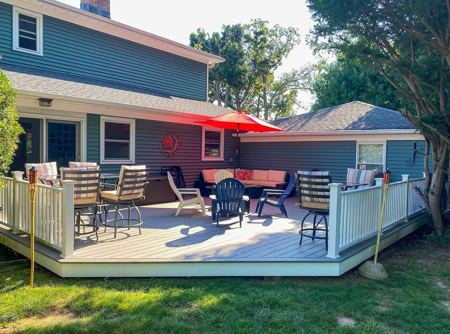 A backyard deck with seating, an umbrella, and a house in the background. Green grass and blue siding.