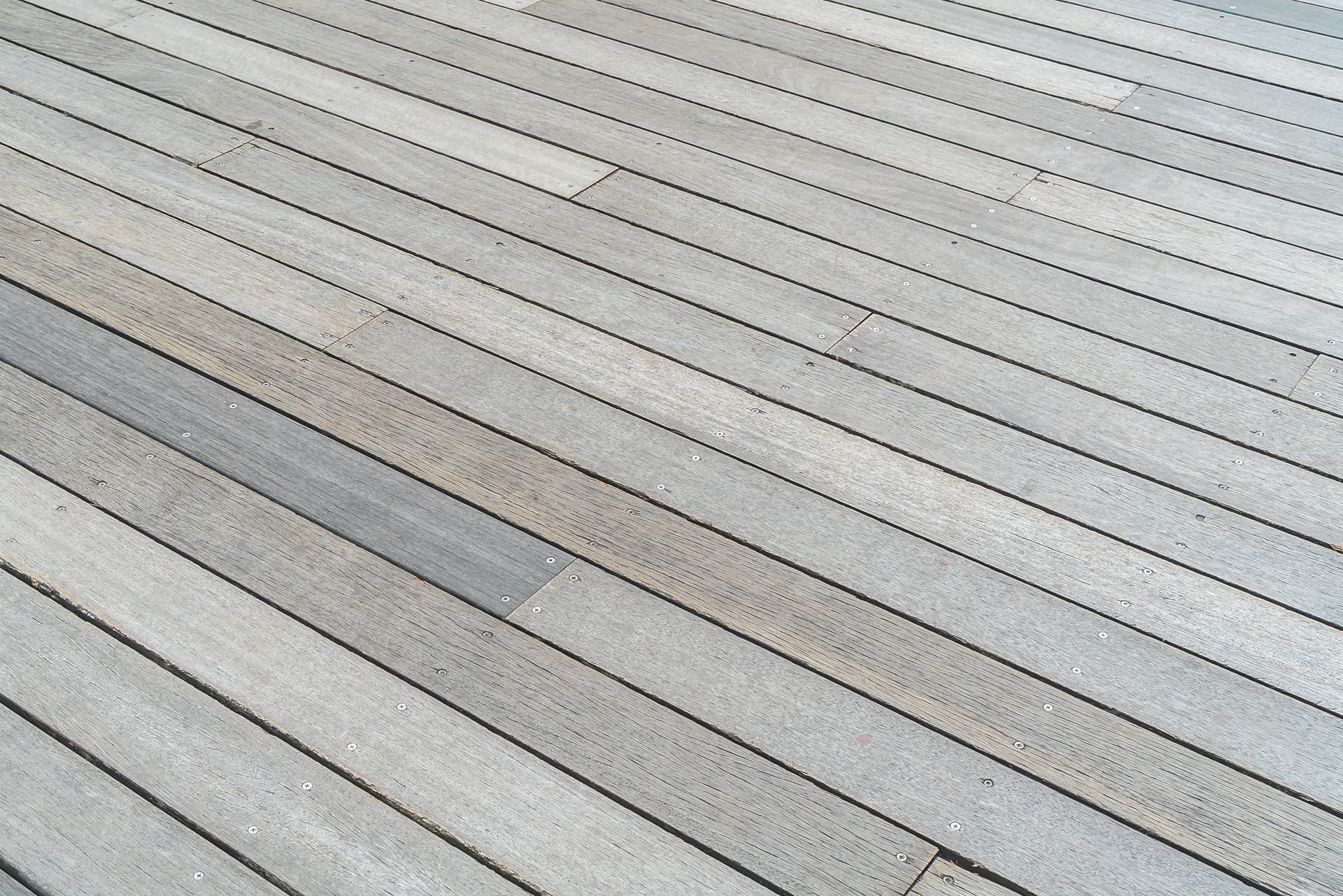 Diagonal view of light gray wooden deck boards with subtle weathering and a darker strip across them
