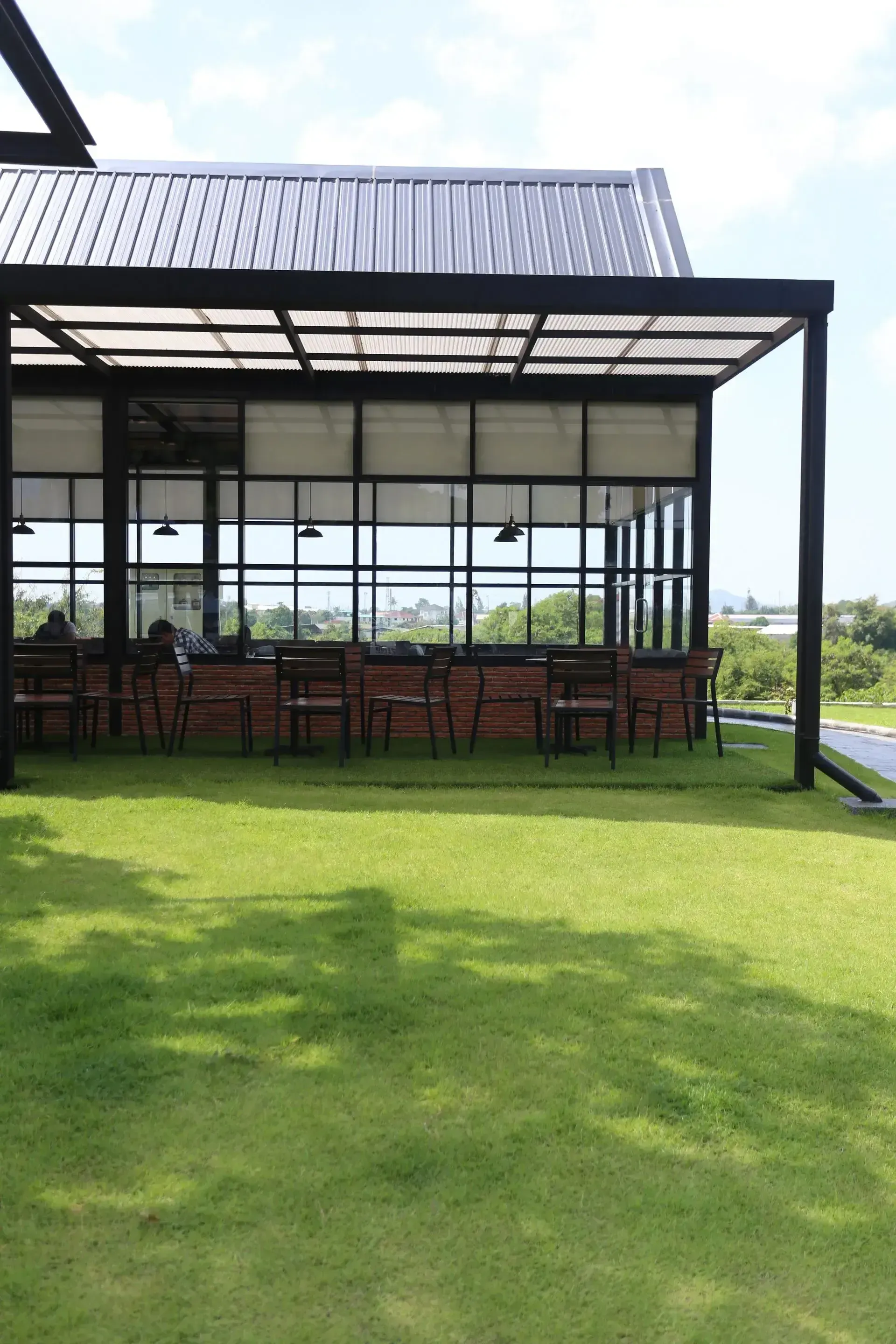A modern building with black frame and glass windows. A lawn is in the foreground.