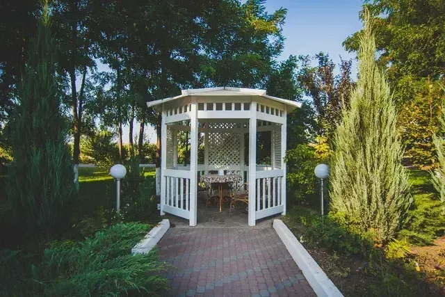 White gazebo with brick path surrounded by greenery.