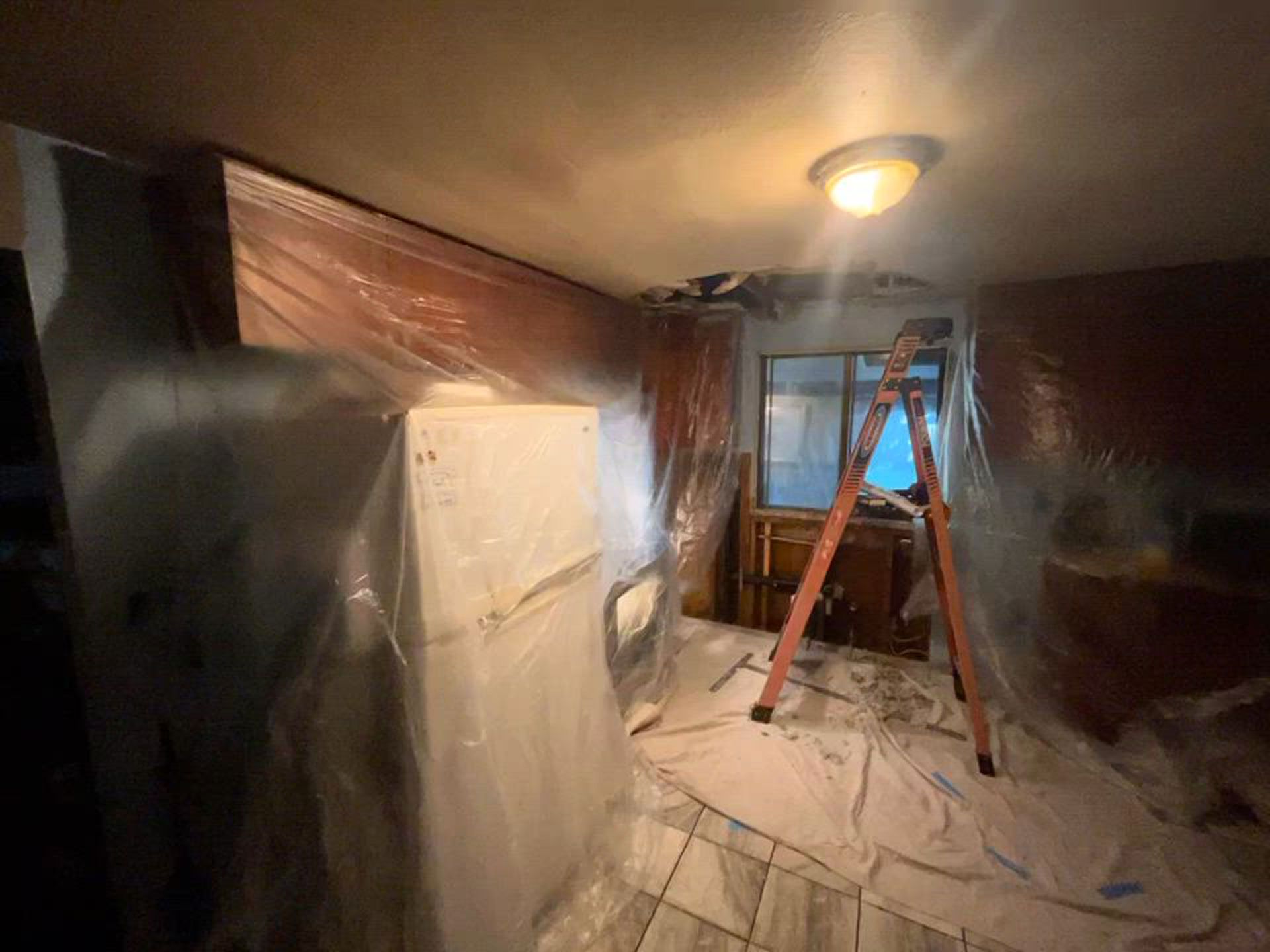 A room with a ladder and a refrigerator covered in plastic