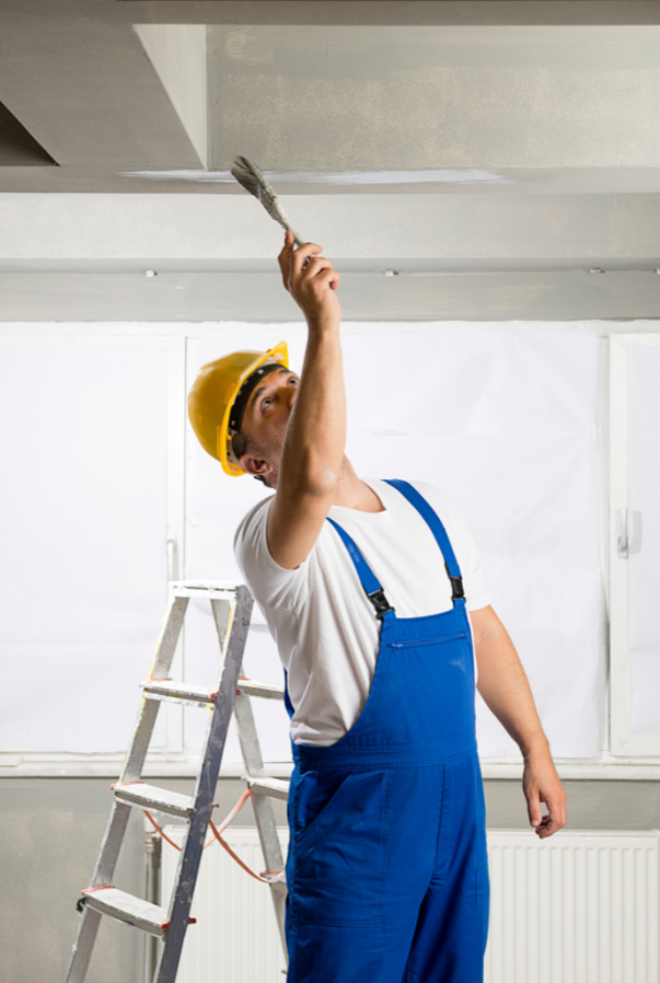A contractor using a paint brush and wearing bib overalls while painting the house's interior.
