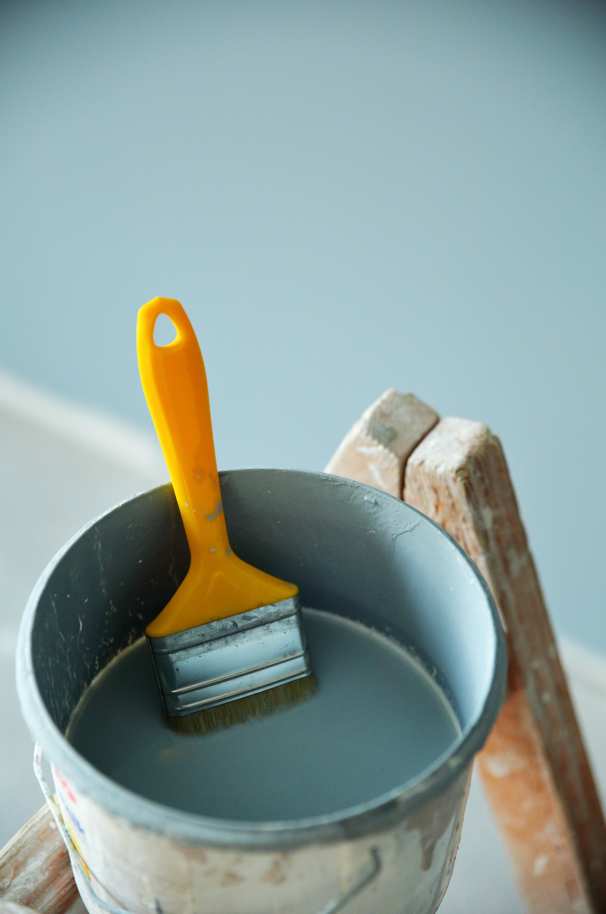 A yellow paintbrush dipped in a bucket of paint.