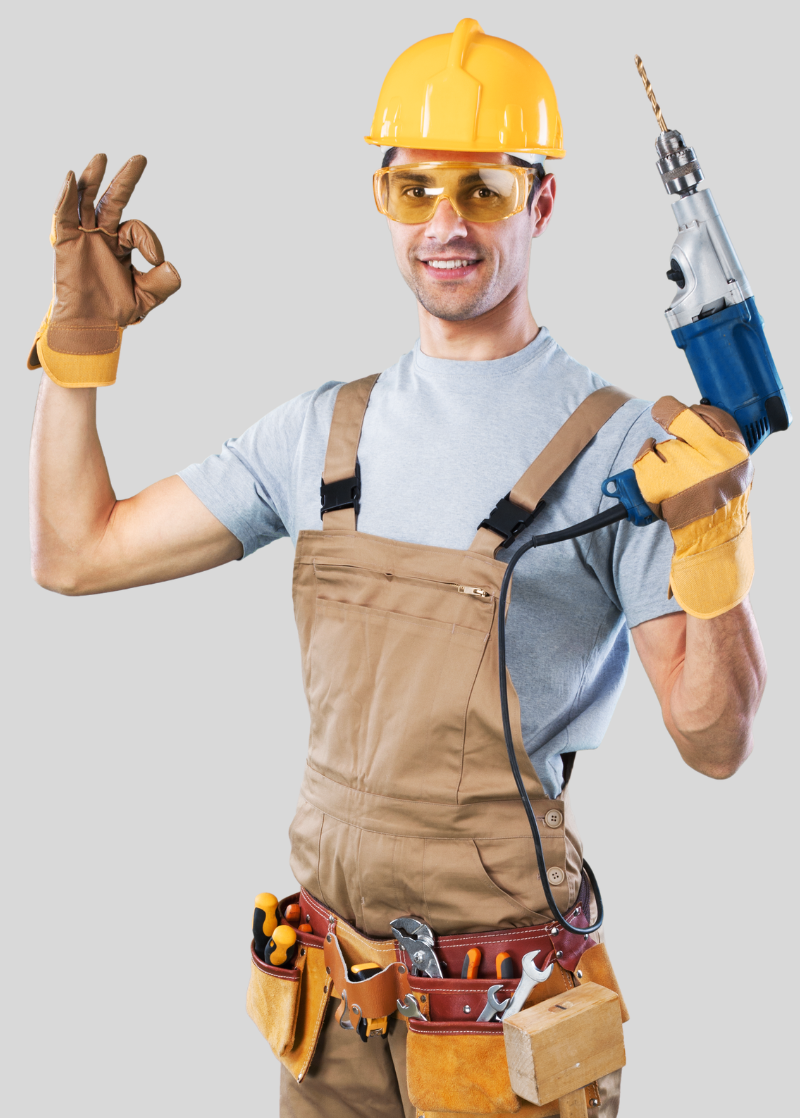 Un homme portant un casque et une salopette tient une perceuse et fait un signe OK.