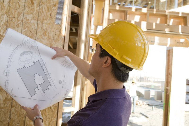 A man wearing a hard hat is looking at a blueprint