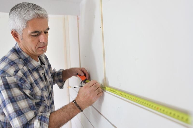 A man is measuring a wall with a tape measure.