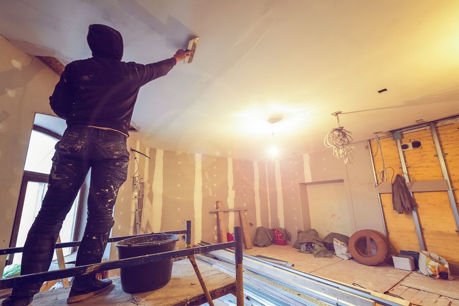 A man is standing on a scaffolding painting the ceiling of a room.