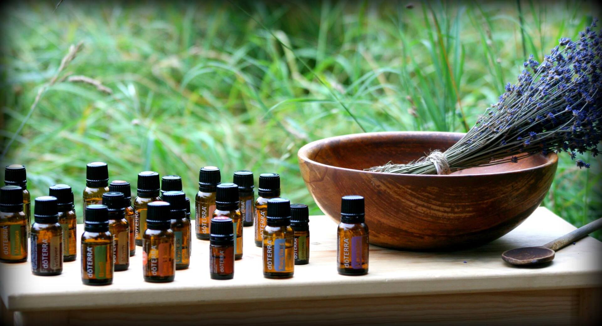 Bottles of essential oils with lavender in a wooden bowl, outside in green grass.