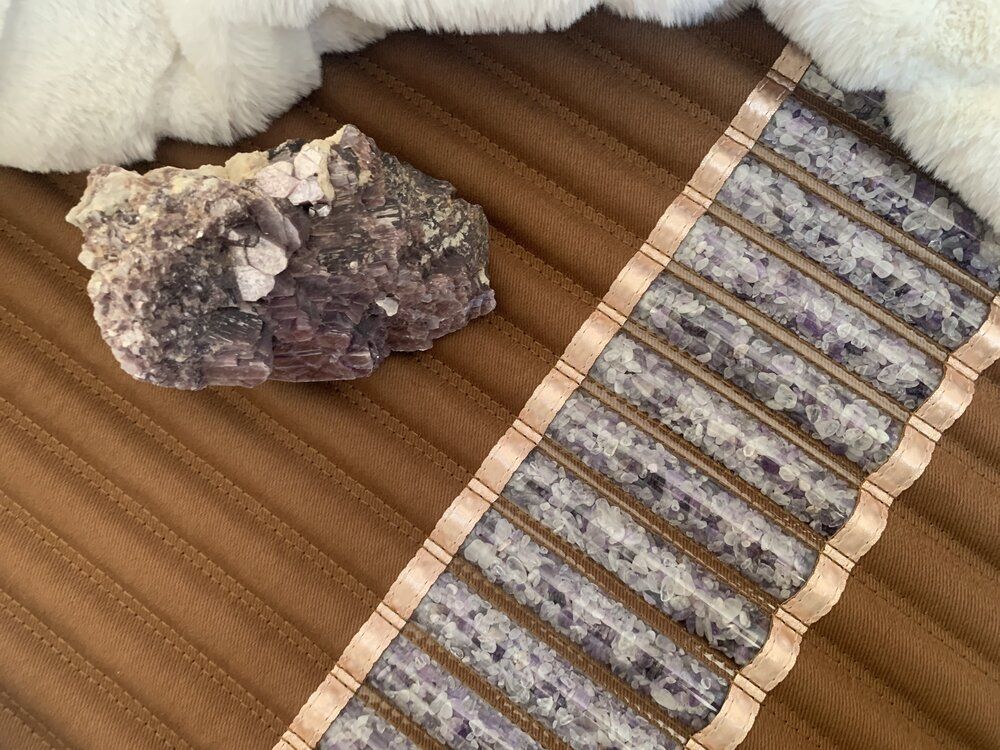 A large, rough purple and white stone next to a brown ribbon and a fluffy white textile on a brown surface.