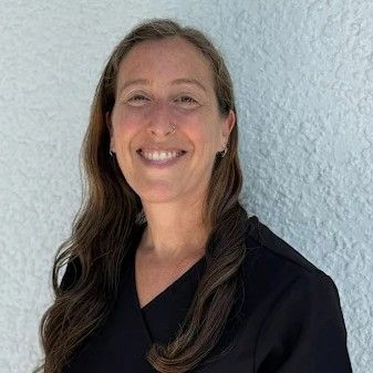 Smiling man with brown hair and stubble in front of a white background. He wears a black shirt.