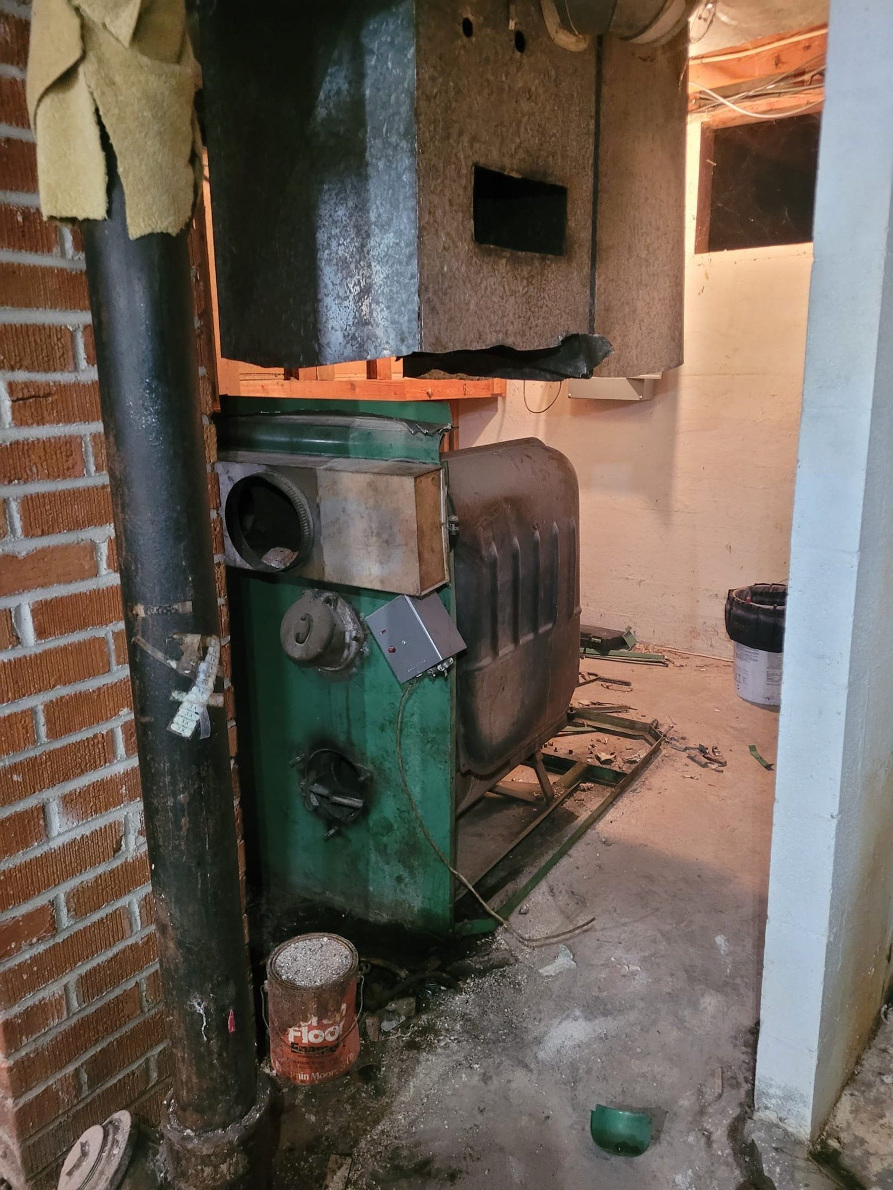 A green boiler is sitting in a room next to a brick wall.