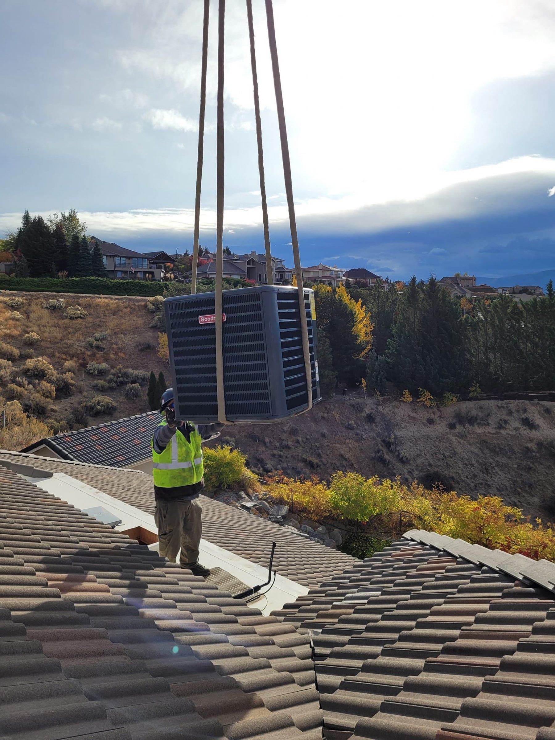 A man is standing on a roof with a crane lifting an air conditioner.