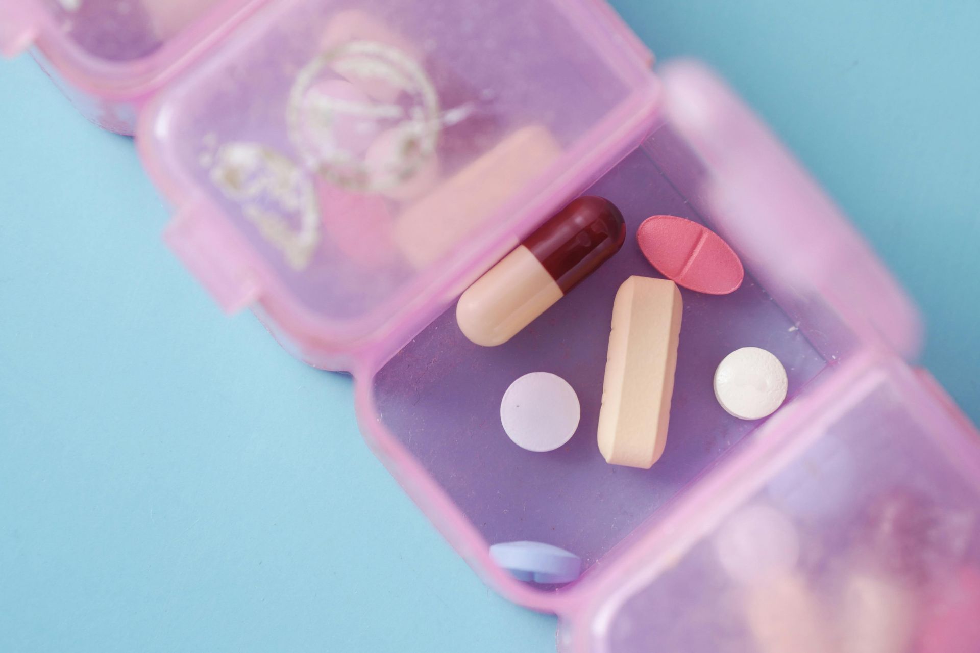 Pink pill organizer with various pills against a blue background.