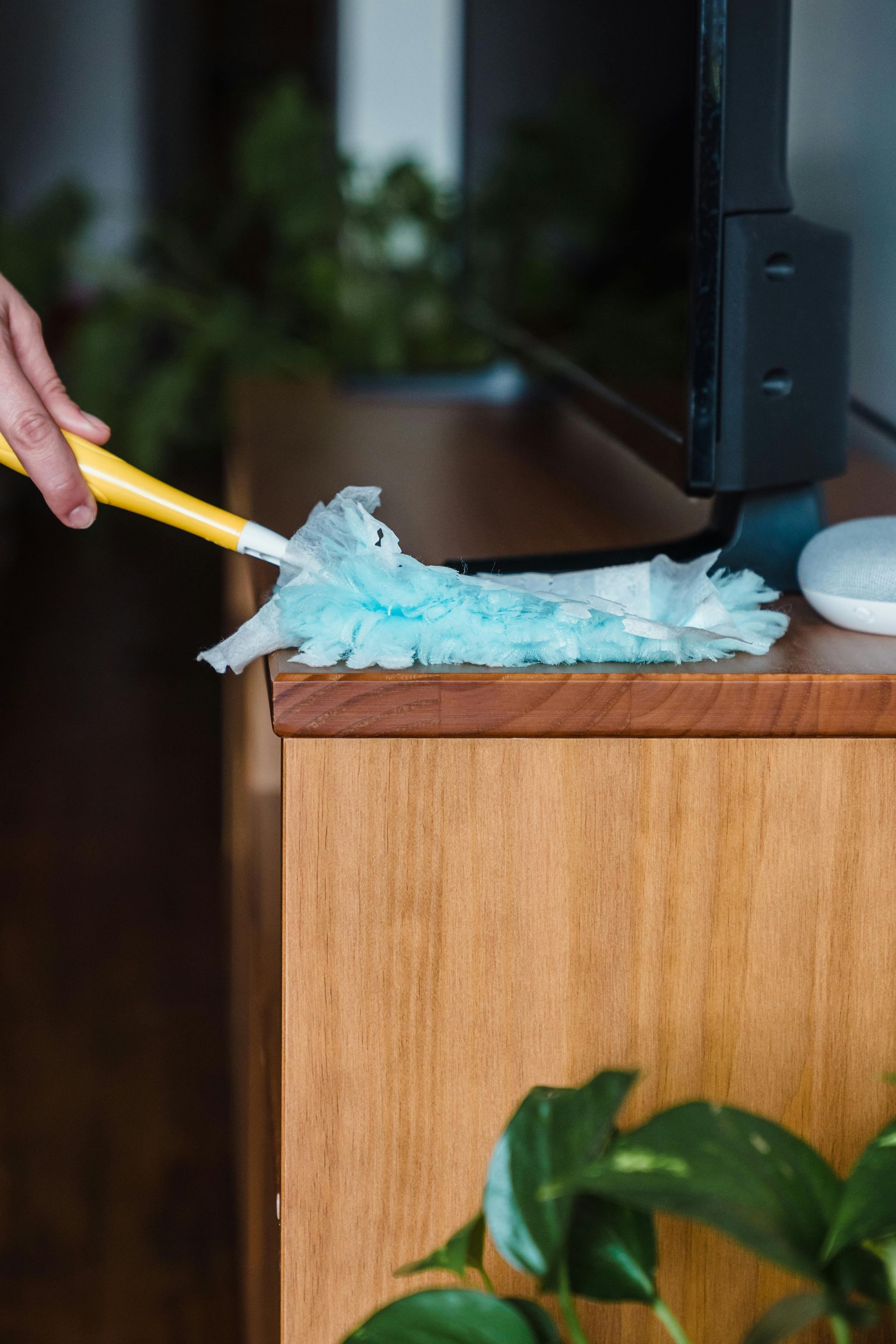 Person dusting a wooden cabinet with a blue and yellow duster.