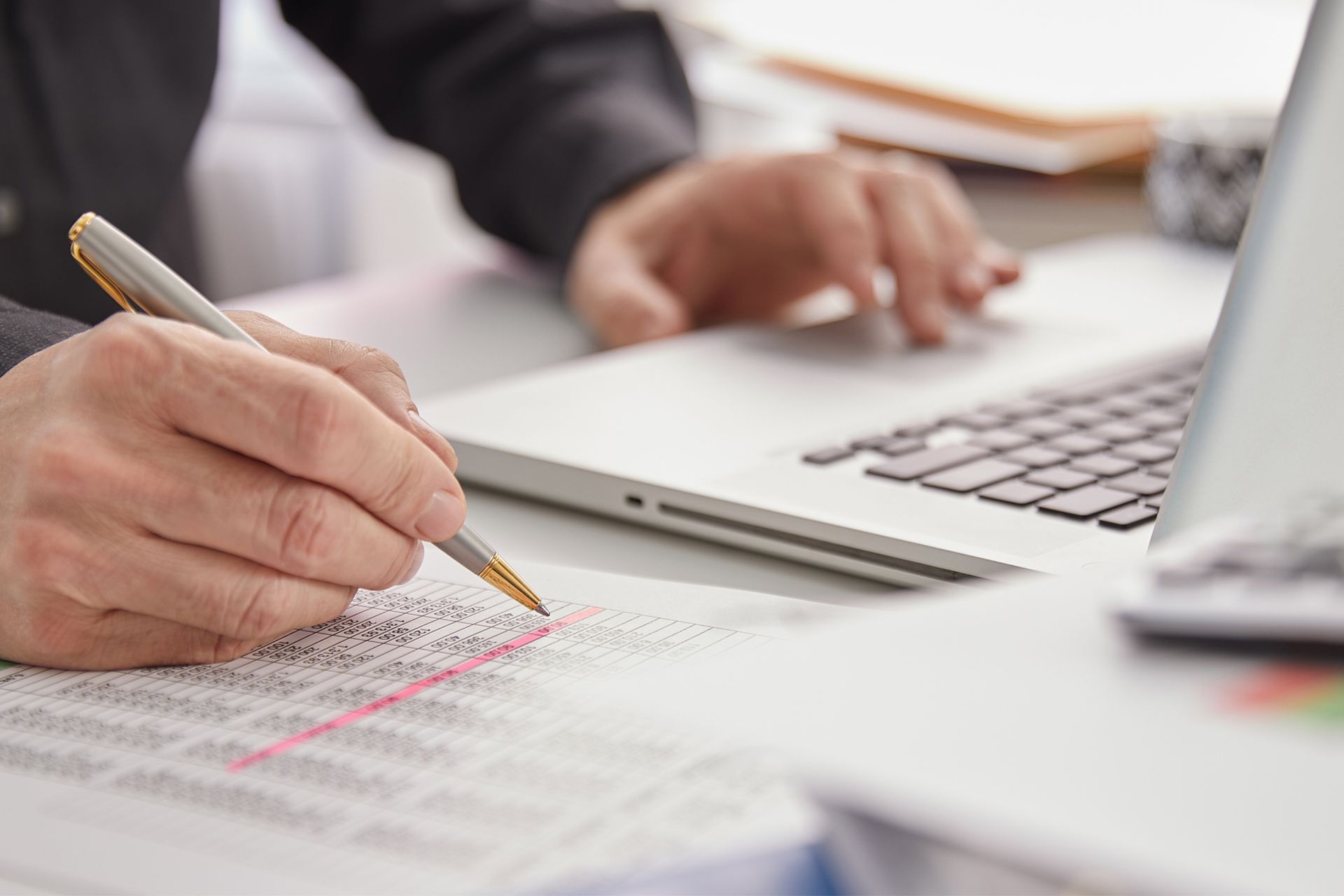 A person is writing on a piece of paper in front of a laptop computer.