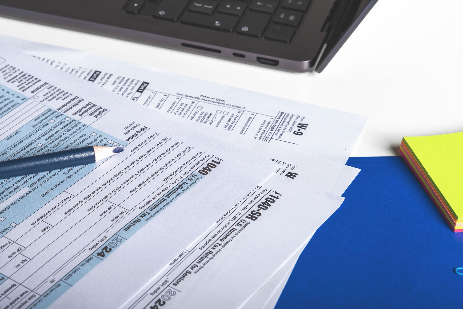 A stack of tax forms next to a laptop A stack of tax forms next to a laptop