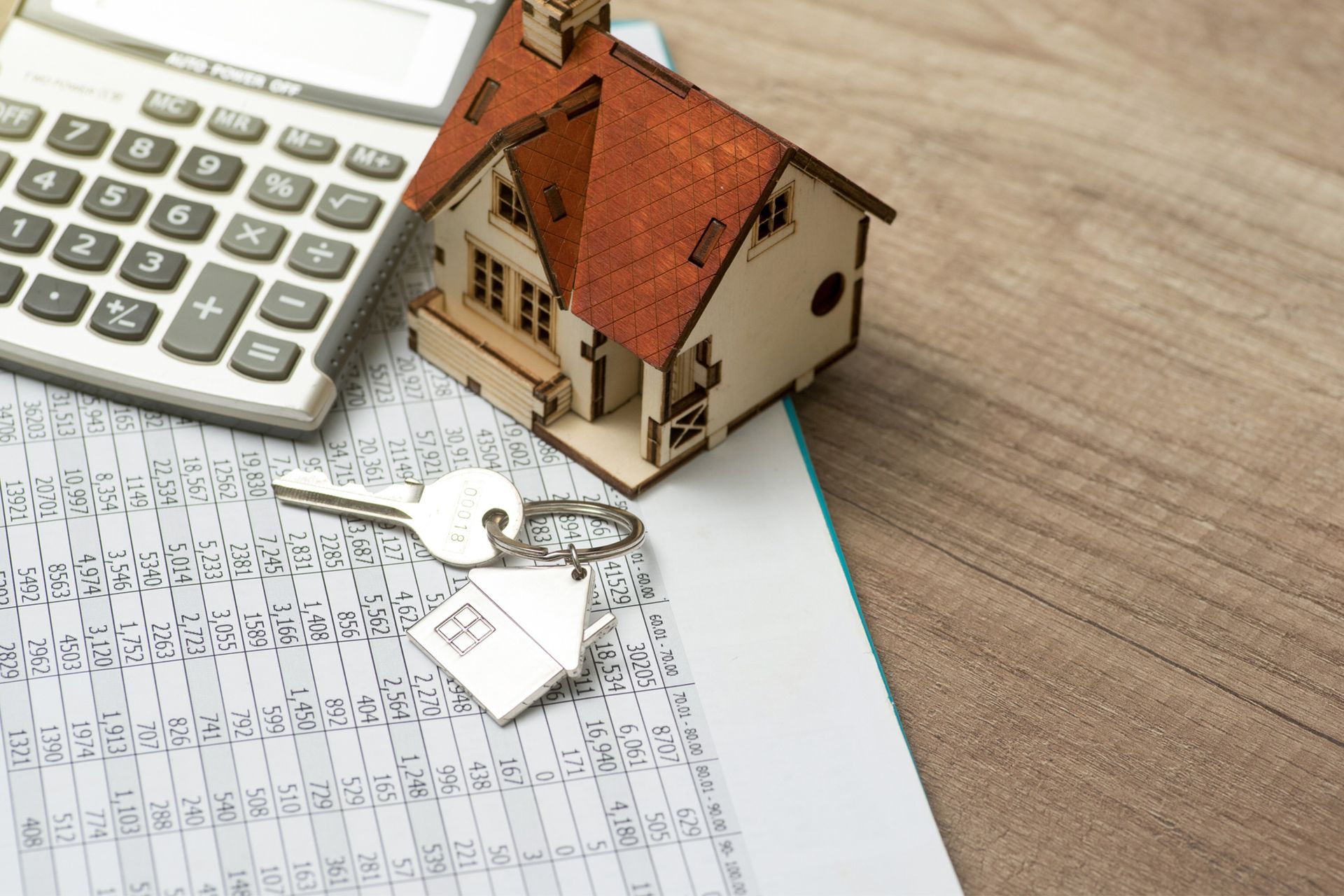 A model house and keys are on a clipboard next to a calculator.