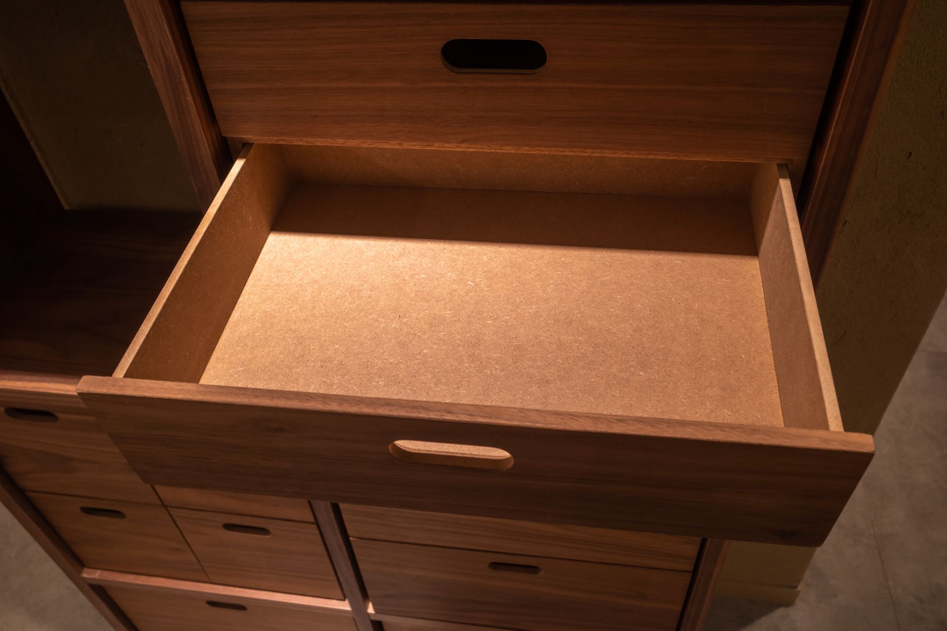 An empty drawer in a wooden cabinet with a handle