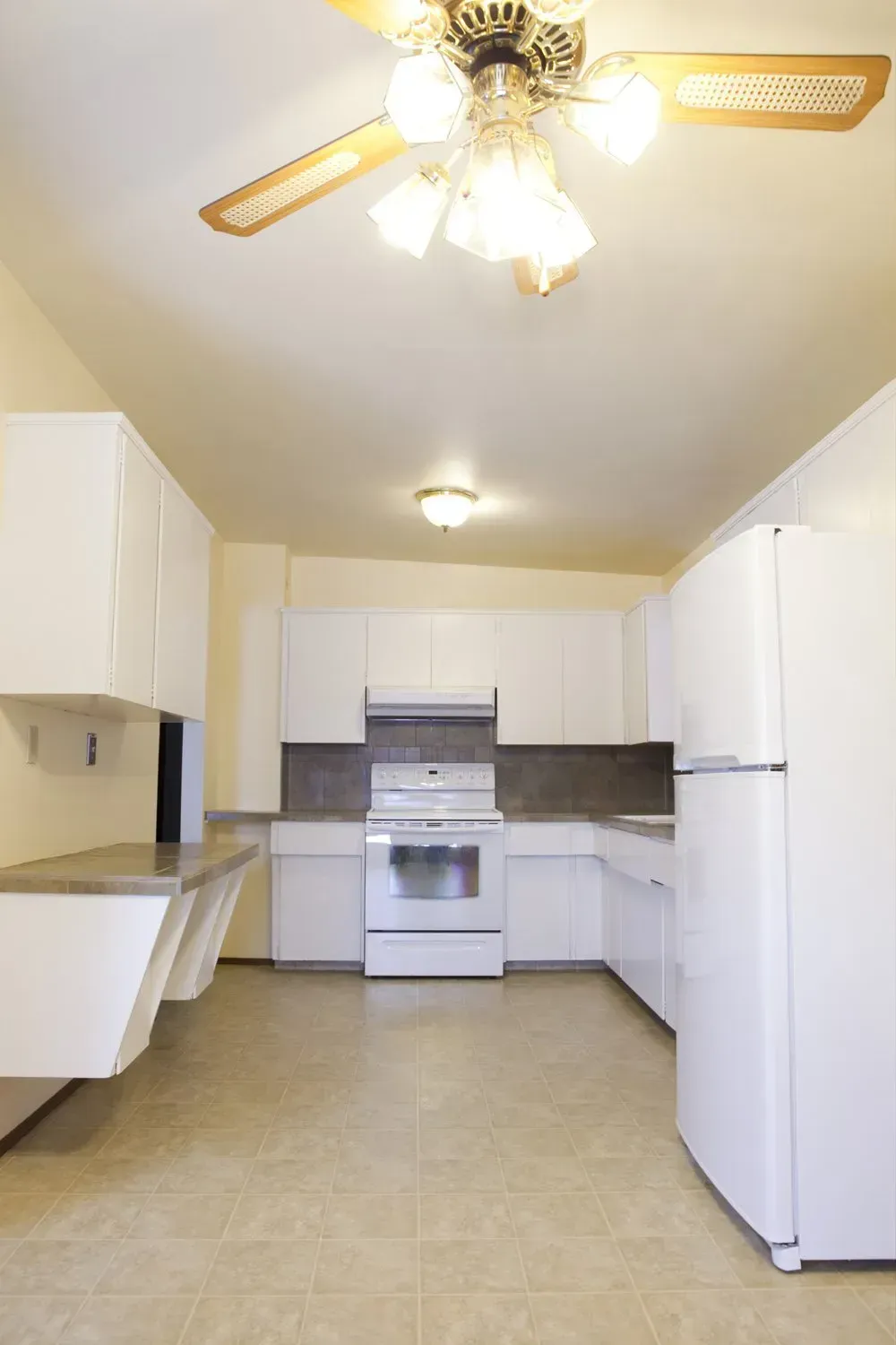 An empty kitchen with white cabinets and a ceiling fan