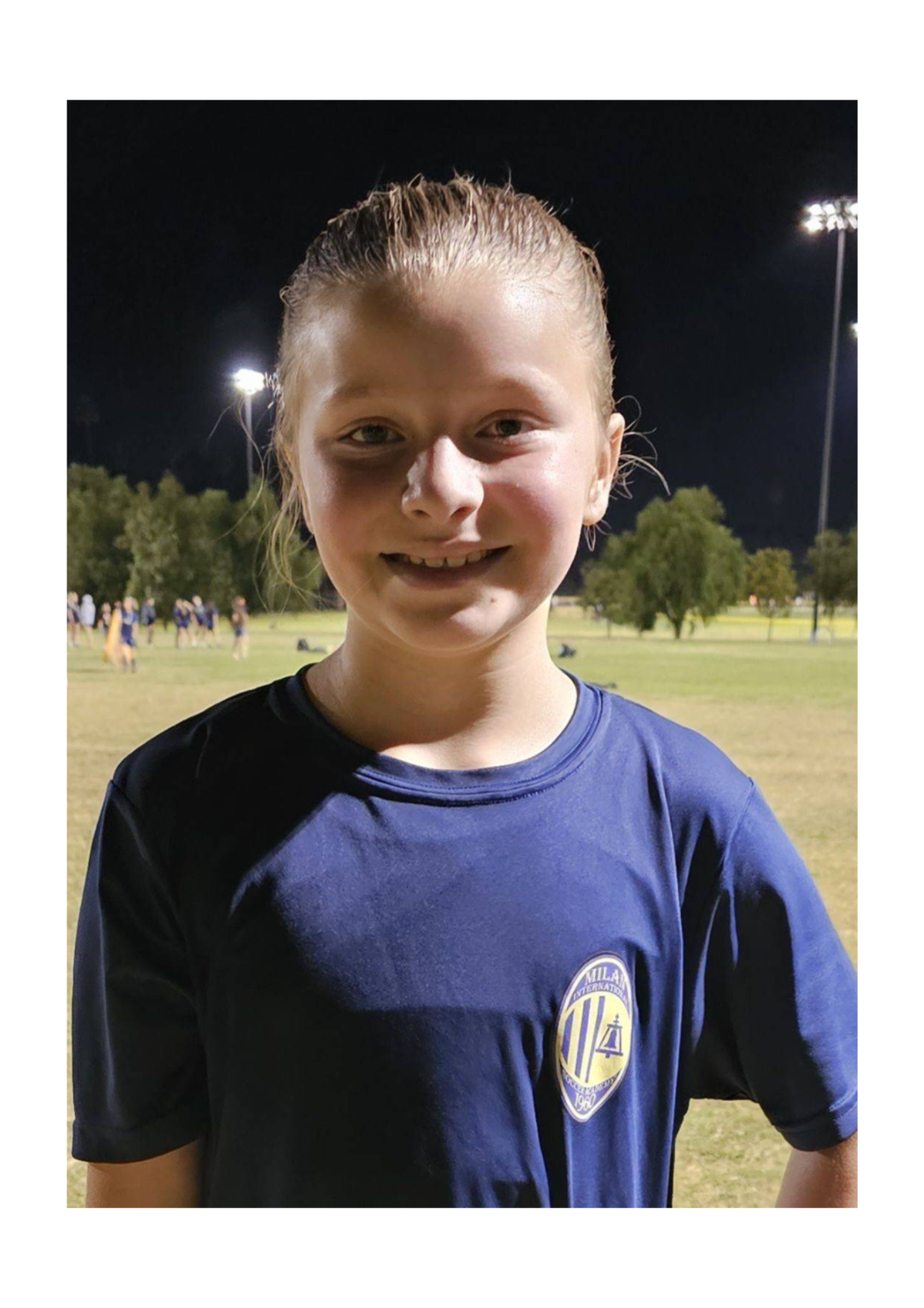 A young girl wearing a blue shirt is standing in a field at night.