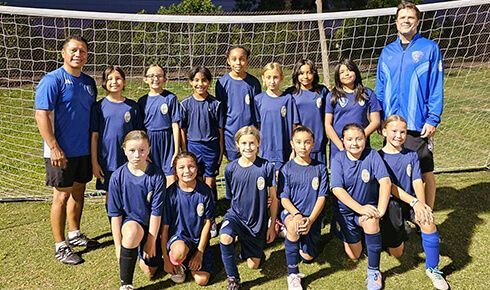 A group of young girls are posing for a picture on a soccer field.