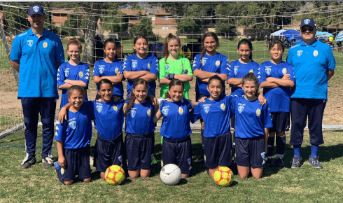 A group of young girls are posing for a picture on a soccer field.