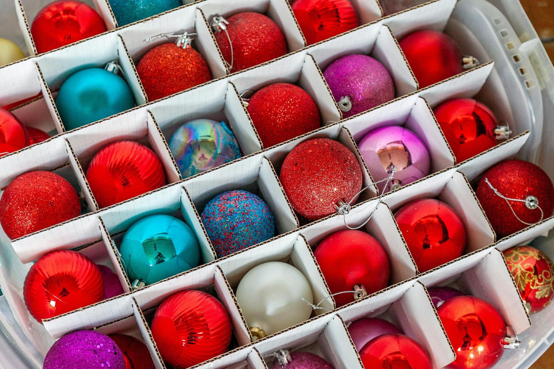 Christmas ornaments in a divided box: red, teal, purple, and white.