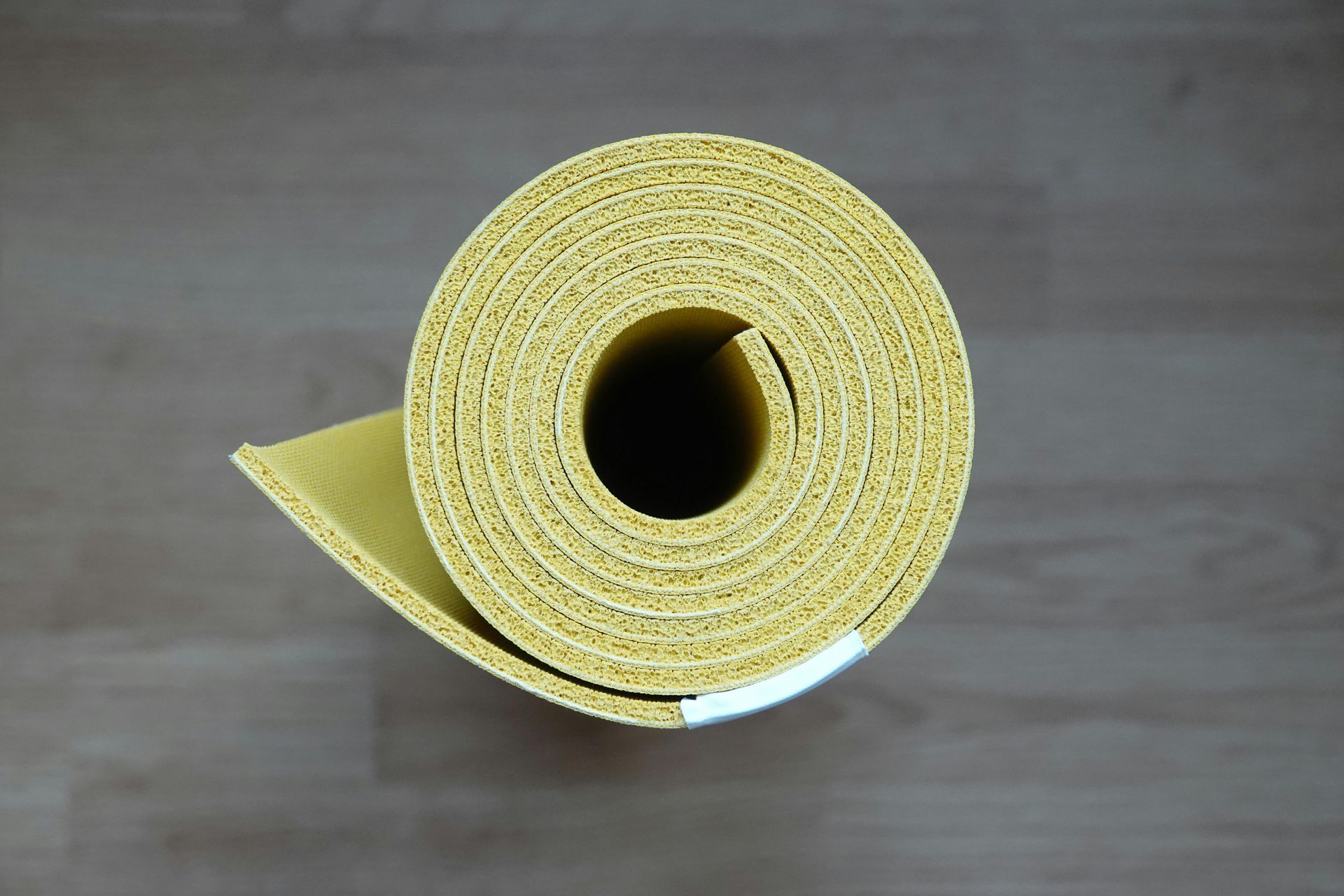 Rolled-up yellow yoga mat on a wood floor.