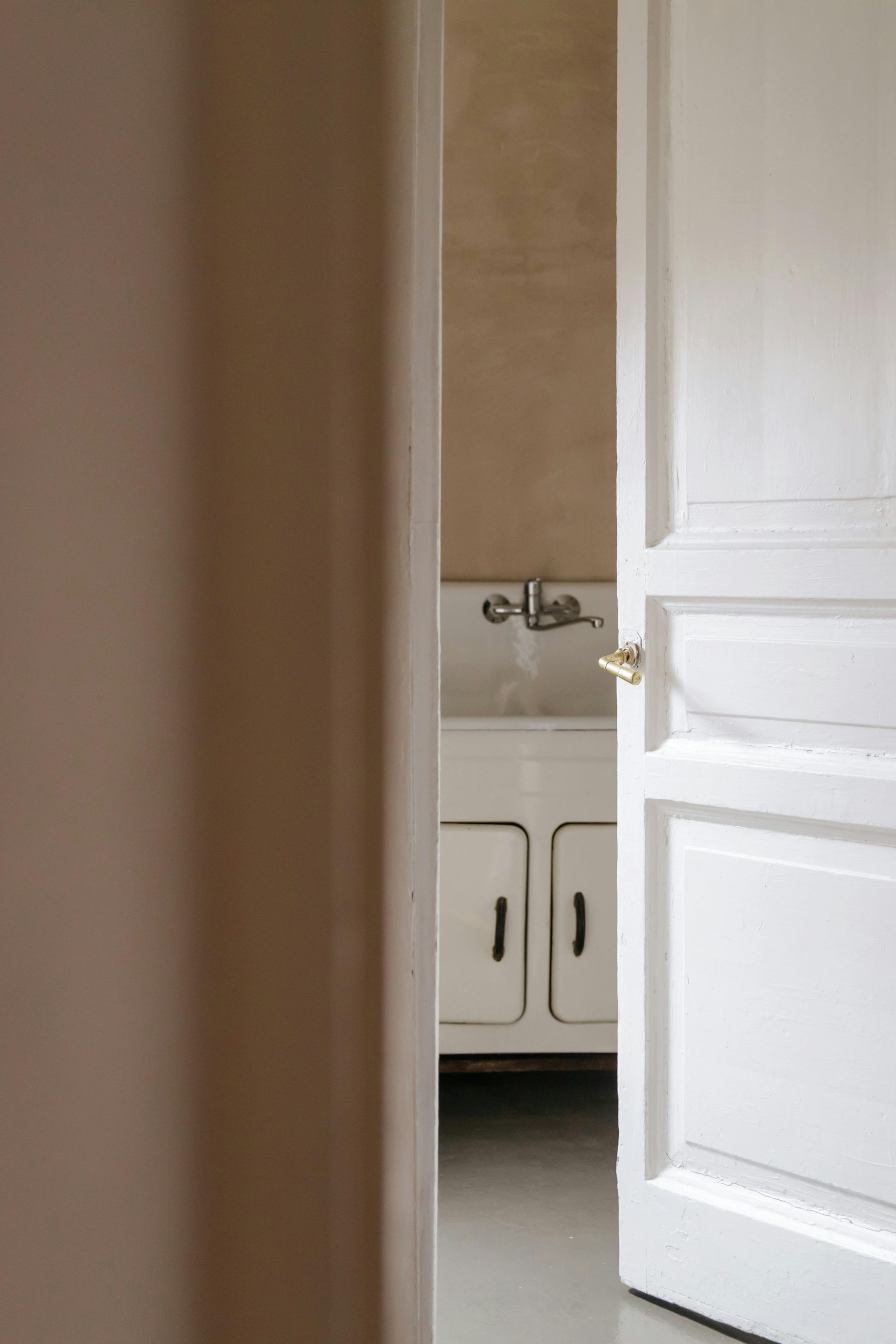An open white door reveals a bathroom with a white vanity cabinet and a wall-mounted faucet.