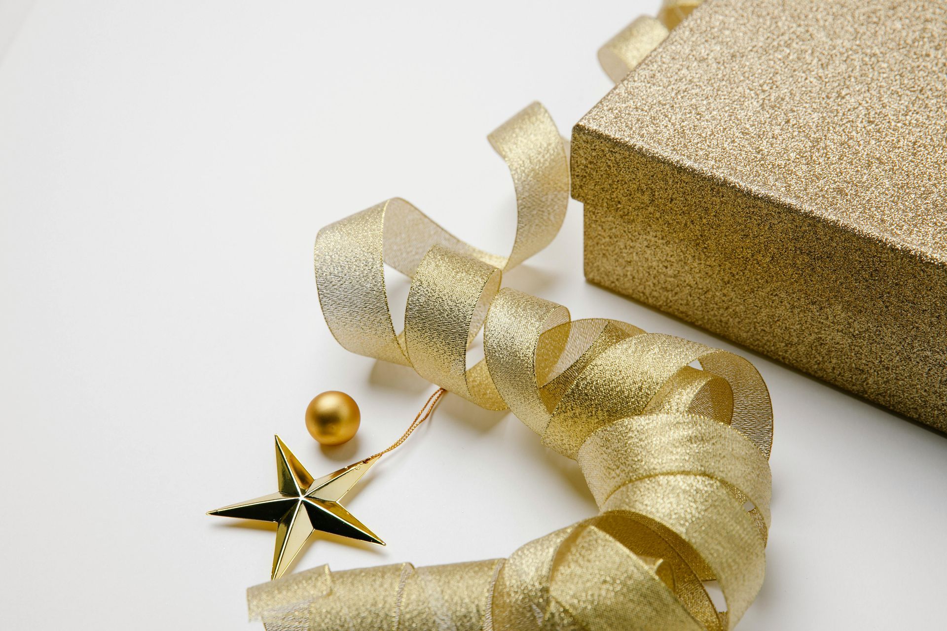 Gold gift box with swirling ribbon, star, and ball ornament on white.