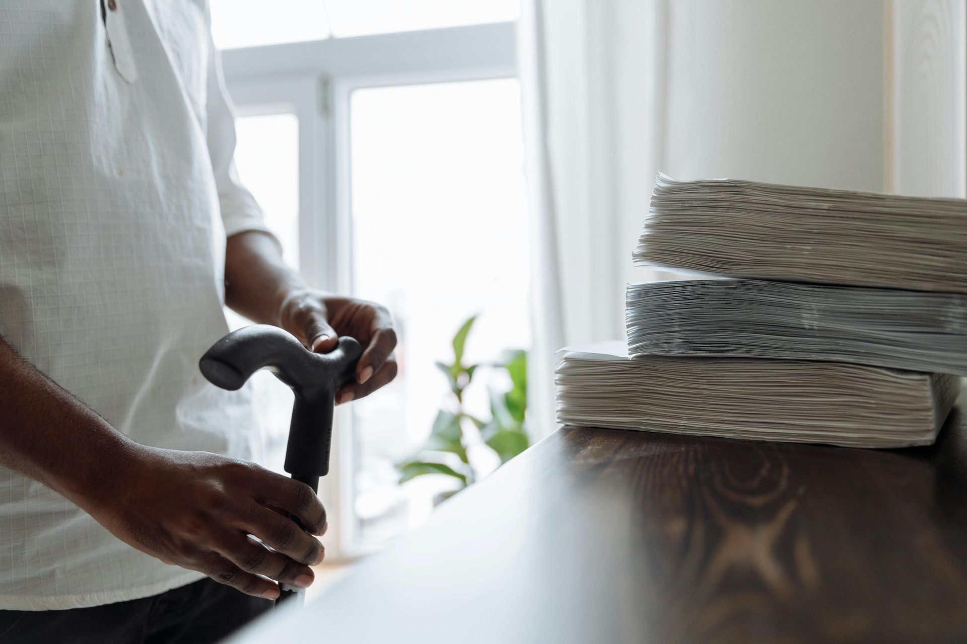 Person with walking cane near stacked papers on a table.