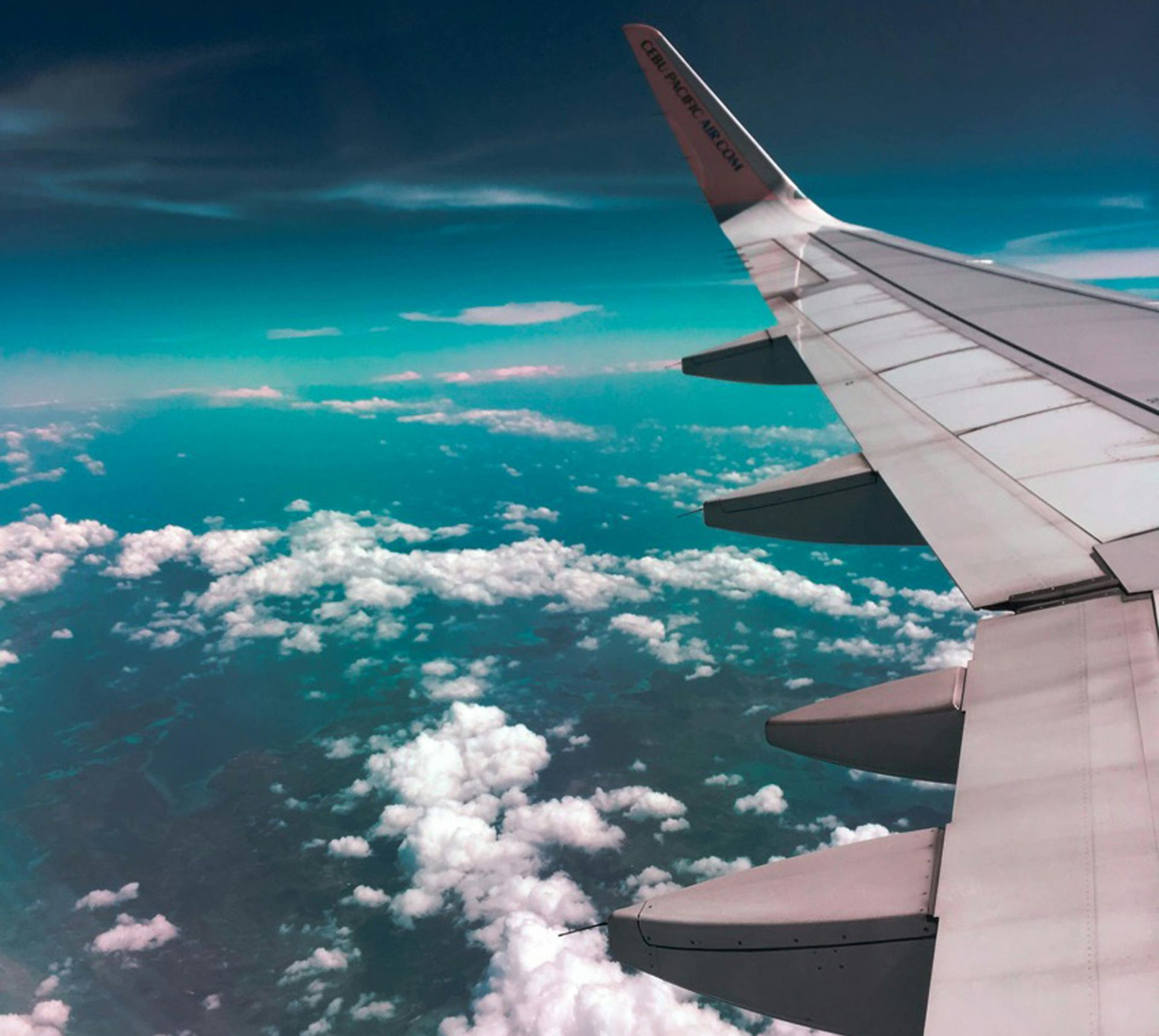 Airplane wing against a backdrop of clouds and teal sky.