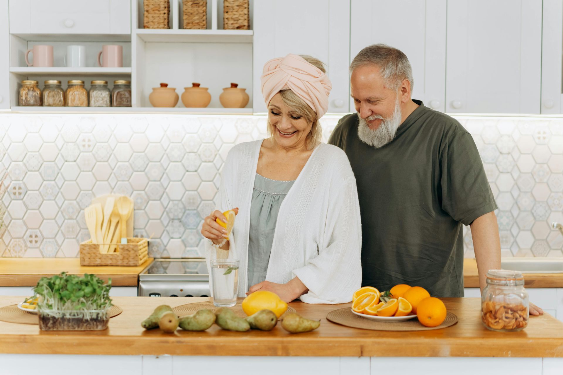 Elderly couple in kitchen preparing fruit and juice, smiling.