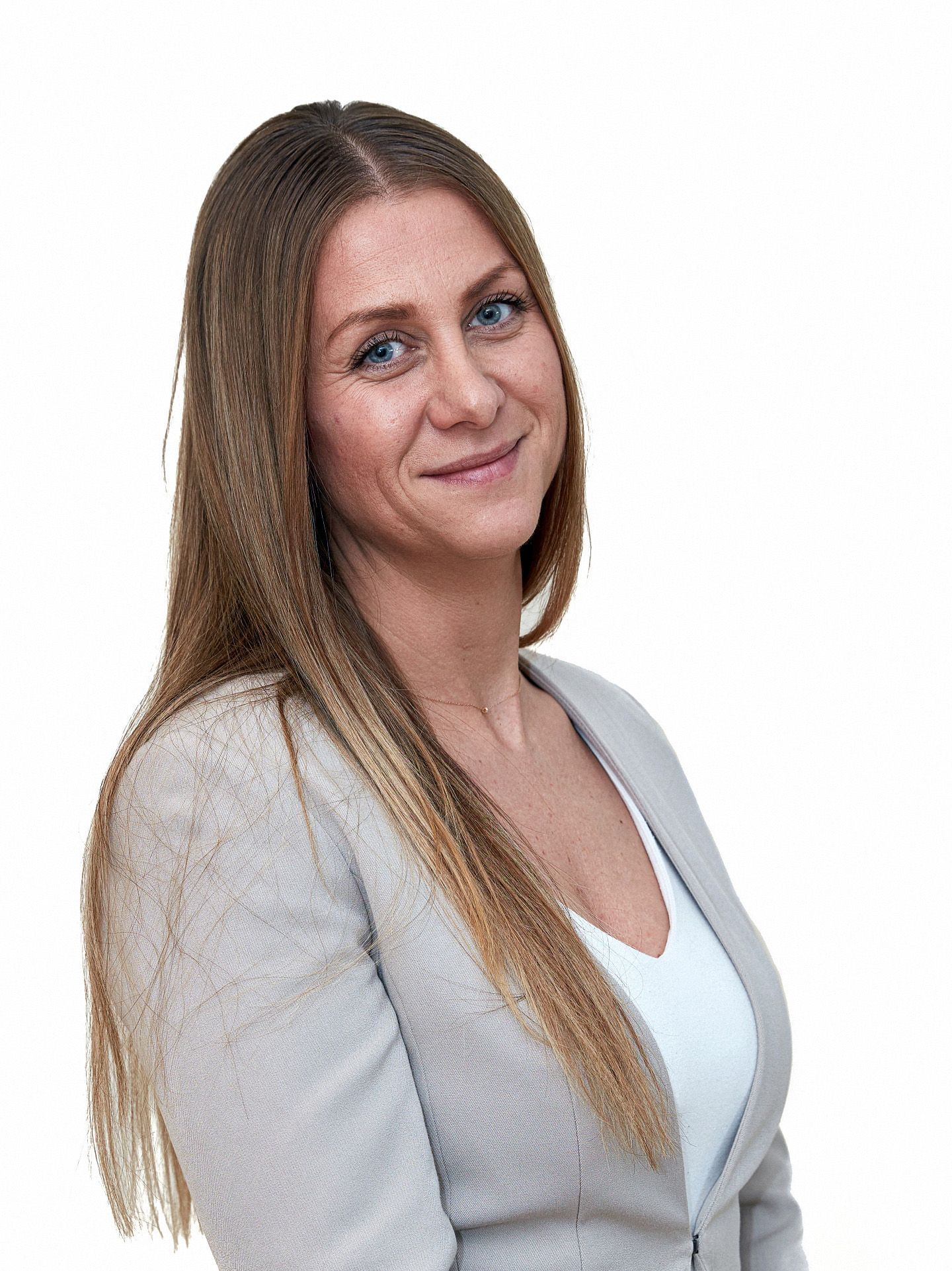 Frau mit langen blonden Haaren, die einen hellen Blazer trägt, lächelt in die Kamera.