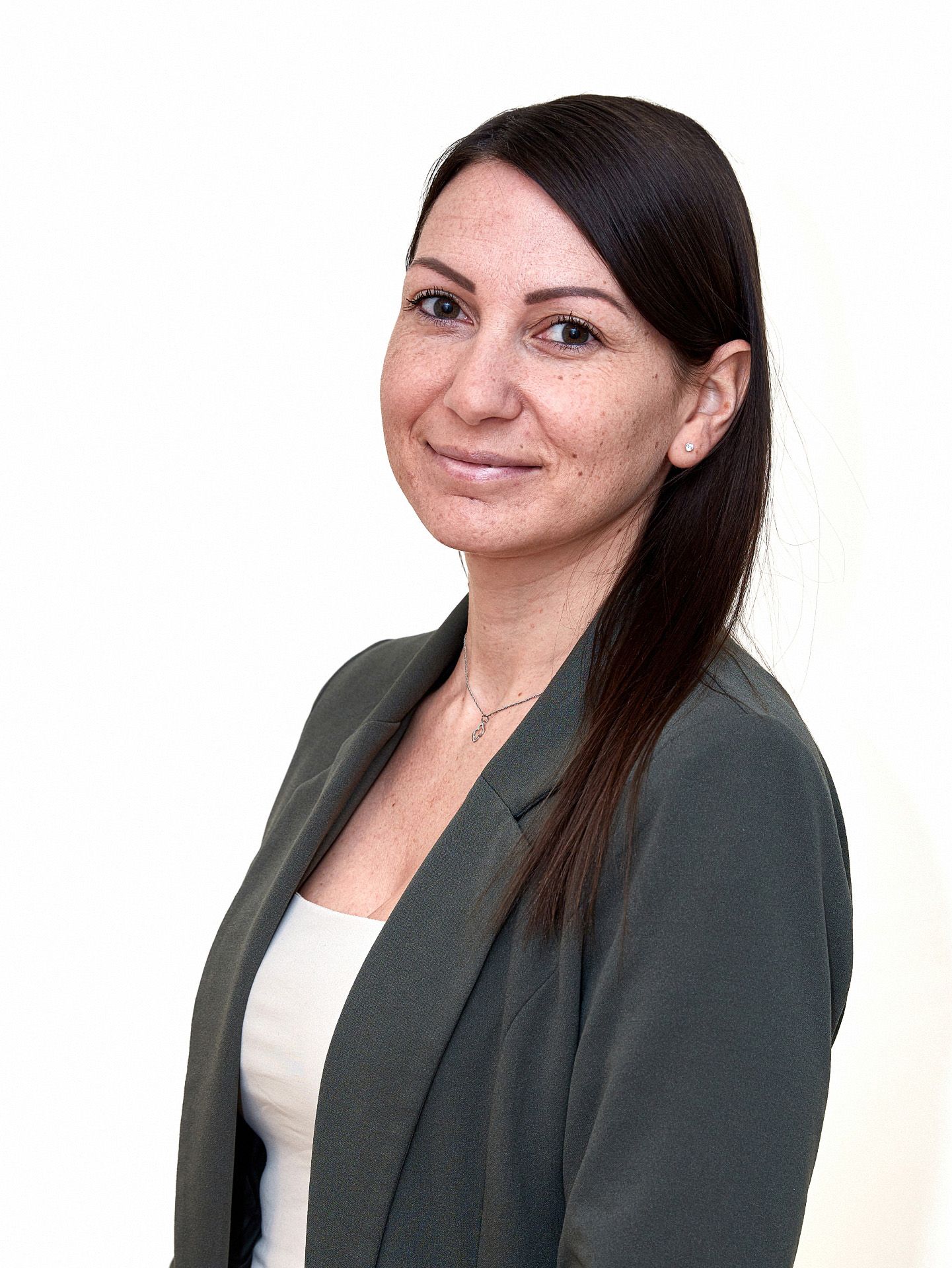 Eine Frau in dunkler Jacke und weißem Oberteil lächelt und blickt dem Betrachter zu.