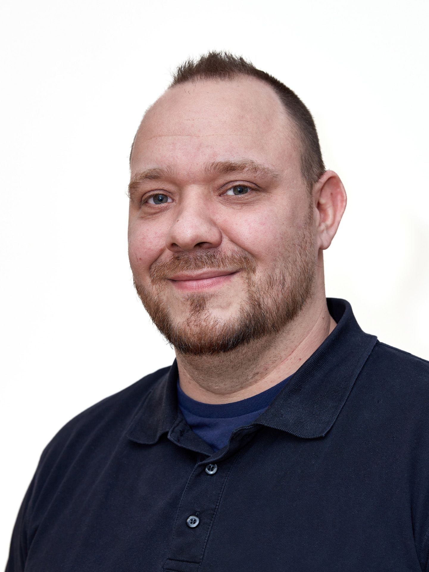 Mann mit kurzem Bart, der ein dunkelblaues Hemd trägt, lächelt und in die Kamera schaut.