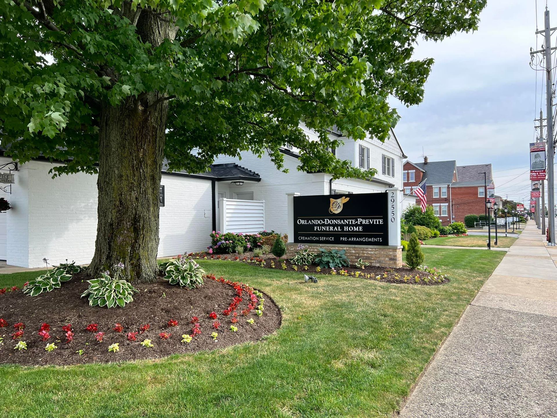 White building with a sign for Orlando-Donsante-Previte Funeral Home next to a large tree and a sidewalk with a street and utility poles.