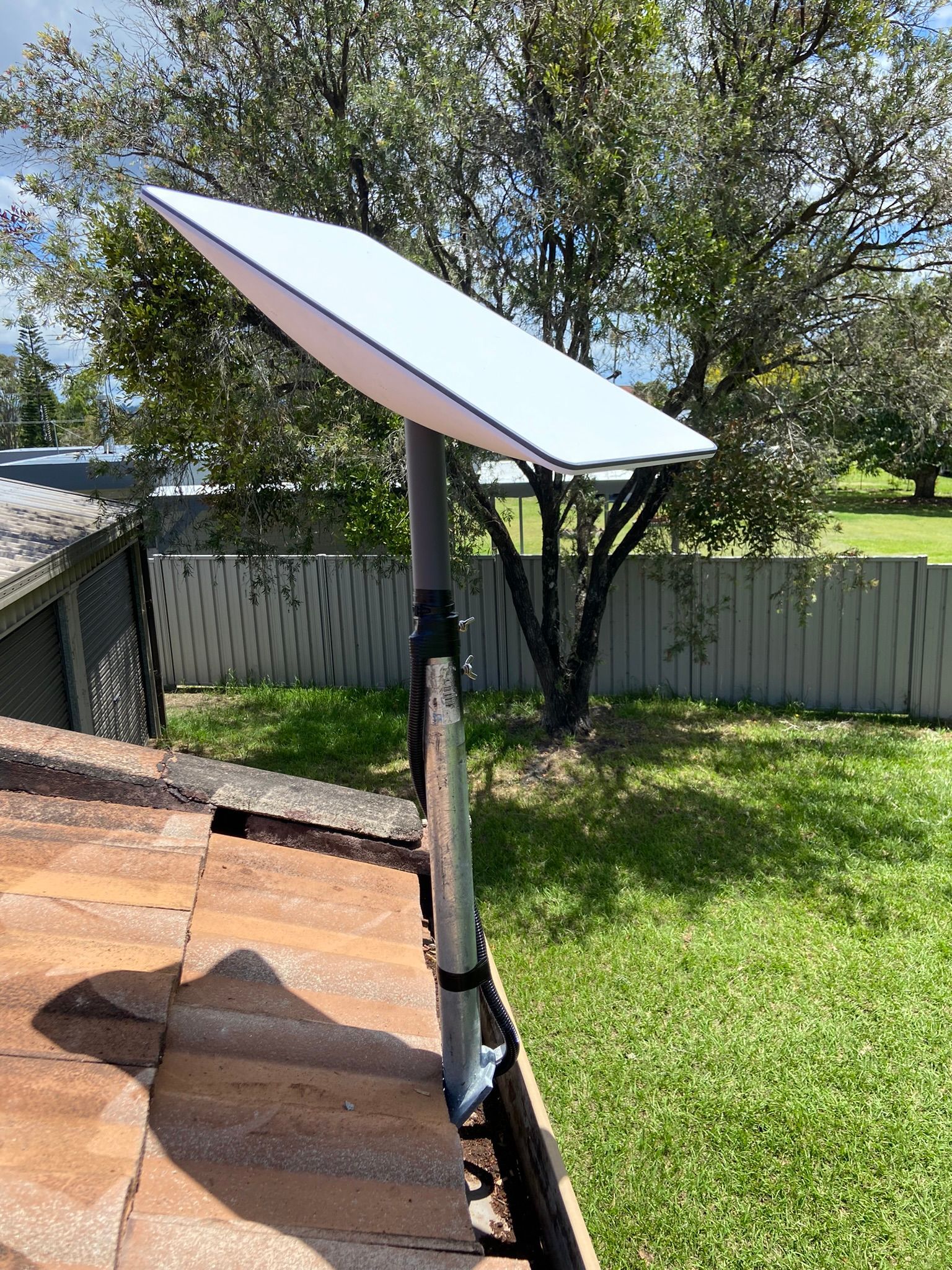 A satellite dish is sitting on top of a roof in a backyard.