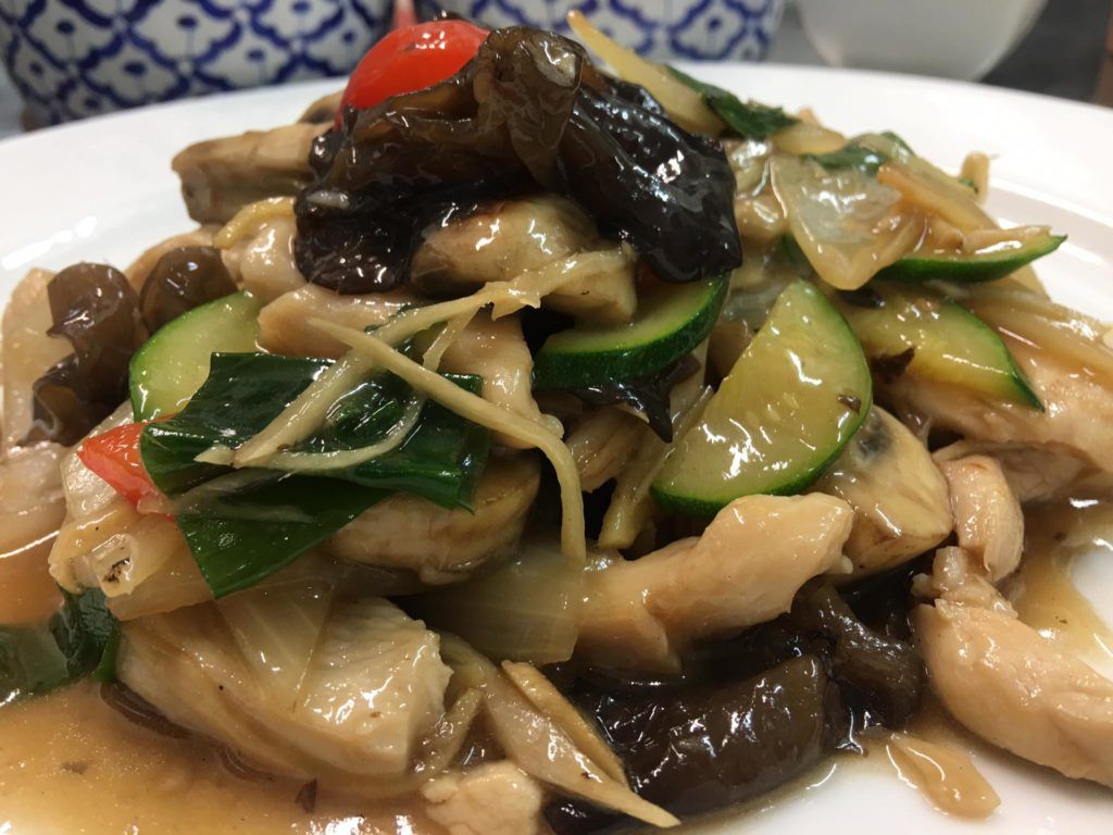 A close up of a plate of food with chicken and vegetables on a table.