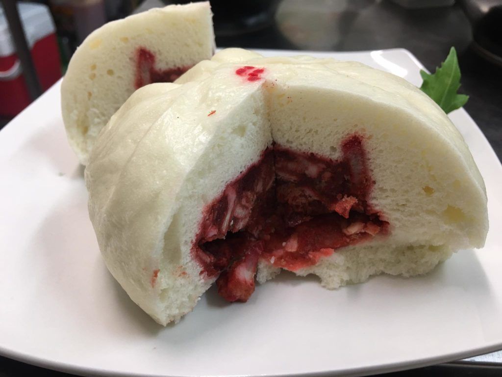 A white plate topped with a strawberry stuffed bun with a bite taken out of it.