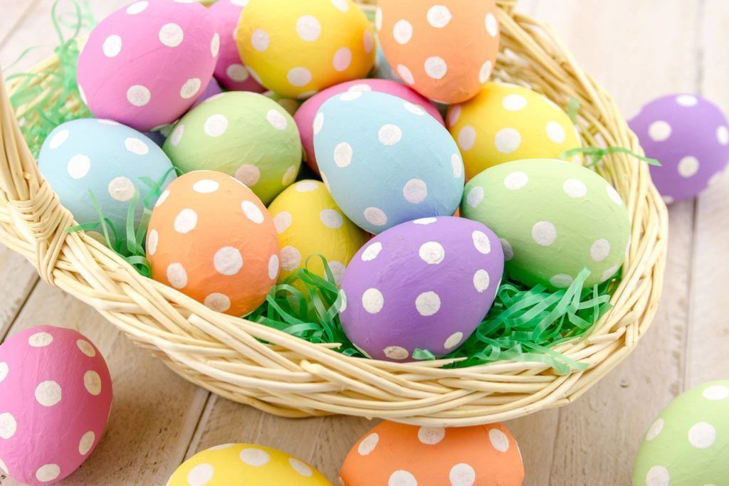 A basket filled with colorful polka dot easter eggs on a wooden table.