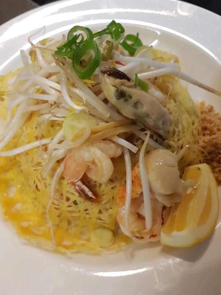 A white plate topped with noodles , shrimp , vegetables and a lemon slice.